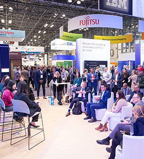 Conférence au salon NRF Big Show avec un public attentif et des stands de grandes marques en arrière-plan.