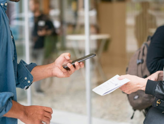 Hand holding a smartphone near an NFC terminal to trigger an action in a retail environment