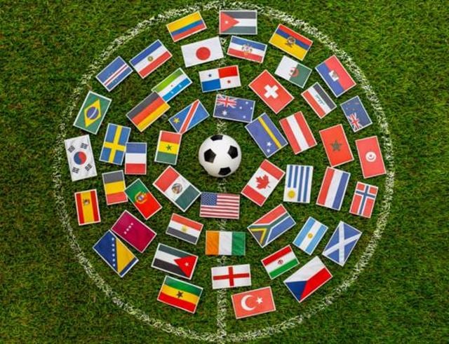 Ballon de football entouré de drapeaux internationaux sur une pelouse de terrain.