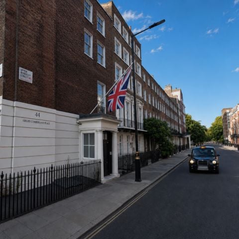 Façade d’un bâtiment londonien avec drapeau britannique sur Great Cumberland Place, sous un ciel bleu, avec un taxi noir circulant dans la rue.