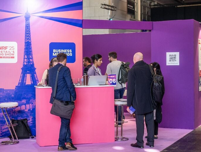 Participants échangeant sur l’espace Business Meetings de NRF 2025: Retail’s Big Show Europe, devant un décor rose avec la tour Eiffel.