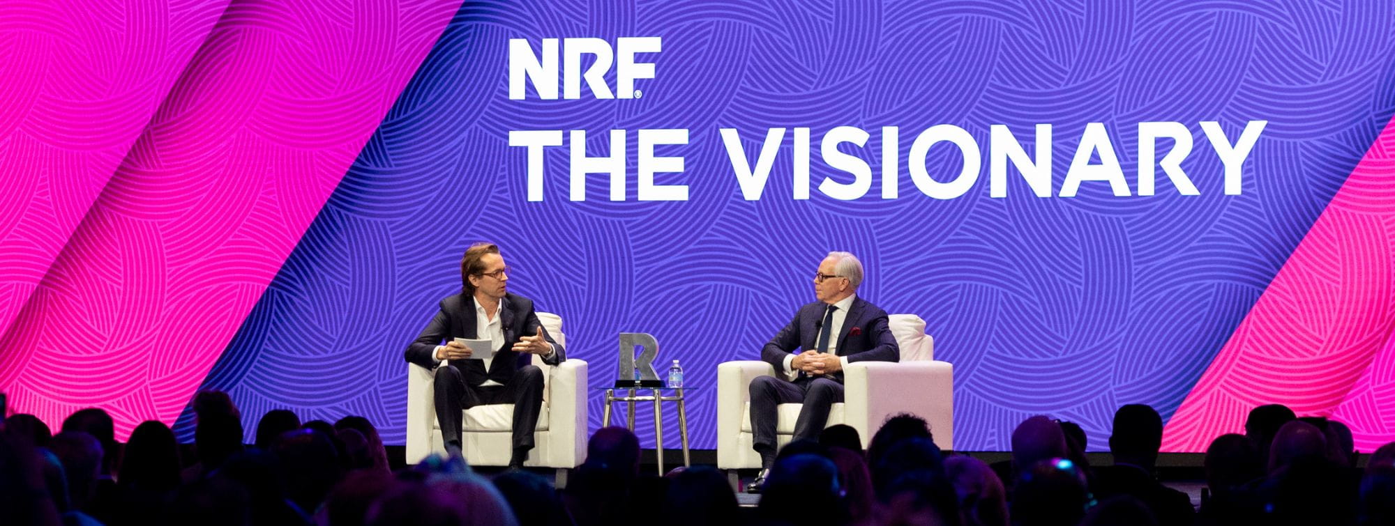 NRF Awards stage featuring two speakers in conversation in front of a “NRF The Visionary” screen, with an engaged audience.