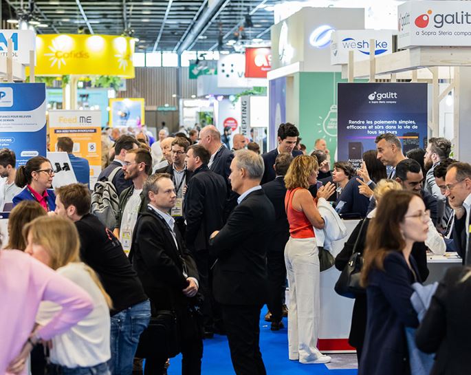  Vue animée des allées d’un salon professionnel avec de nombreux visiteurs en discussion autour des stands d’exposants.