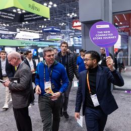 Guided tour at NRF 2025, a speaker holds a sign "The New Connected Store Journey" leading a group through the exhibition area.