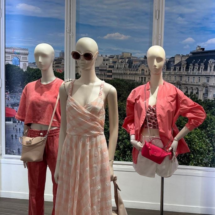 Mannequins dressed in summer outfits in front of a window with a view of the Arc de Triomphe and Paris rooftops.