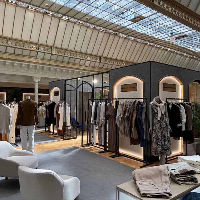 High-end boutique space with a glass roof, elegant furniture, and Brunello Cucinelli clothing racks.