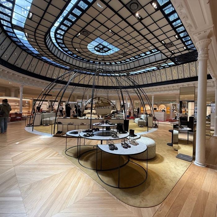 Interior of a Parisian department store with a glass dome and fashion products displayed under a modern design structure.